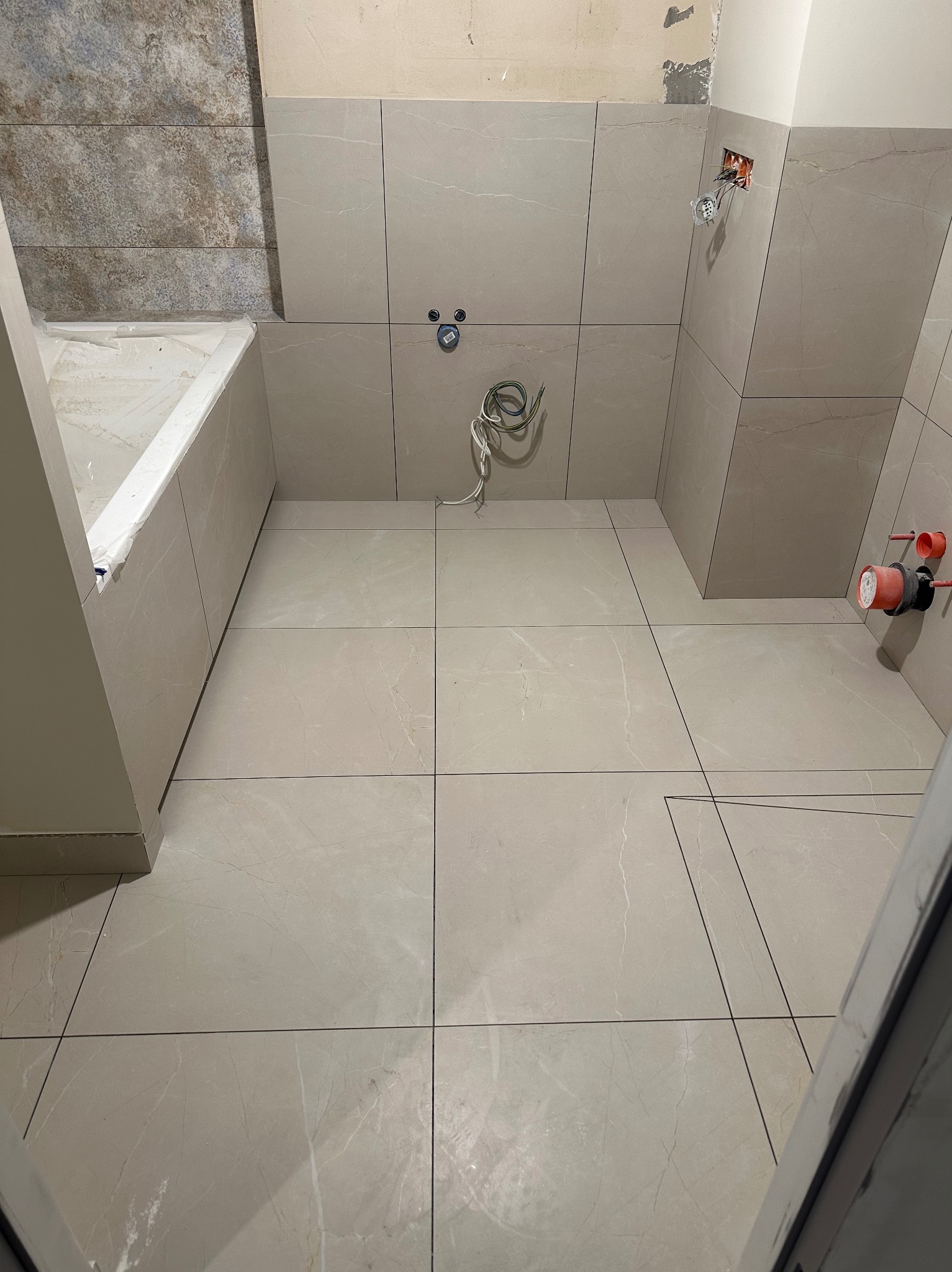 Wykończona beżowa łazienka w Radzyminie z wanną i płytkami imitującymi marmur, widoczne instalacje wodne i elektryczne, gotowa do dalszych prac.