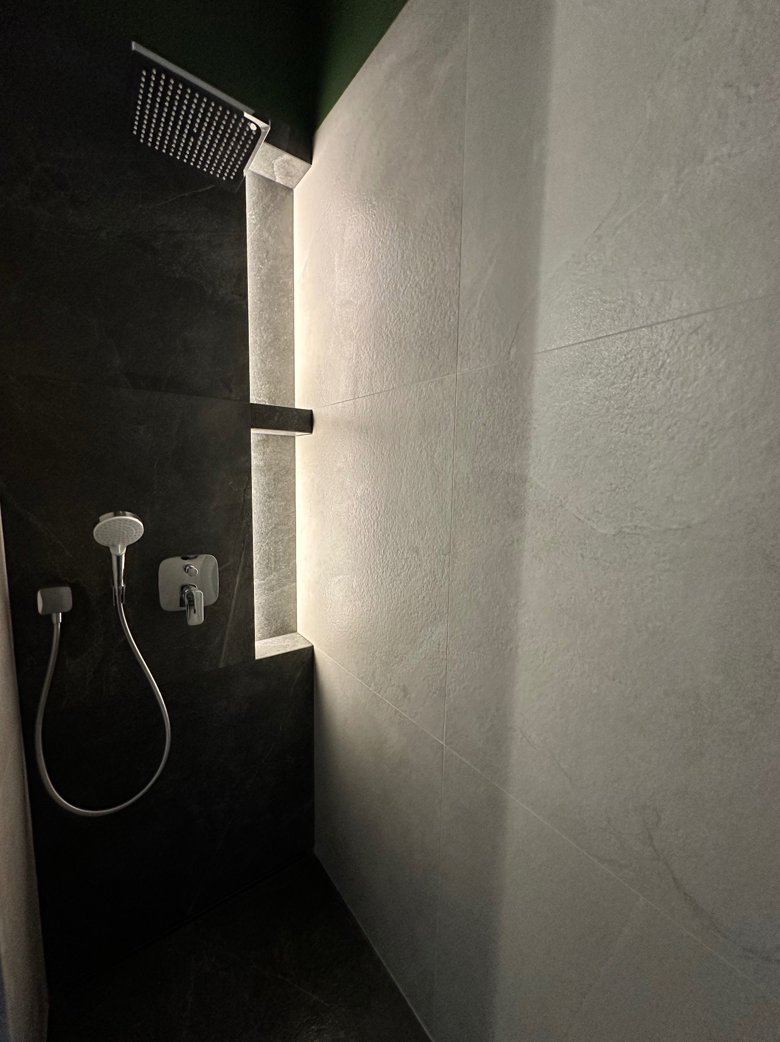 Nowoczesna kabina prysznicowa z czarnymi i szarymi płytkami, oświetloną wnęką i deszczownicą, prezentująca minimalistyczny design łazienki.