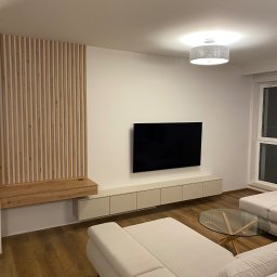 PROEFEKT Michał Czaplicki - Nowoczesny salon w Warszawie z drewnianą ścianką działową, podwieszaną szafką RTV i minimalistycznym oświetleniem sufitowym nad narożną sofą.
