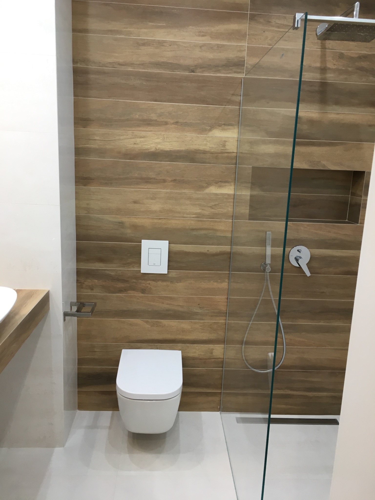 Nowoczesna łazienka z drewnopodobnymi płytkami, kabiną prysznicową typu walk-in i podtynkową toaletą.