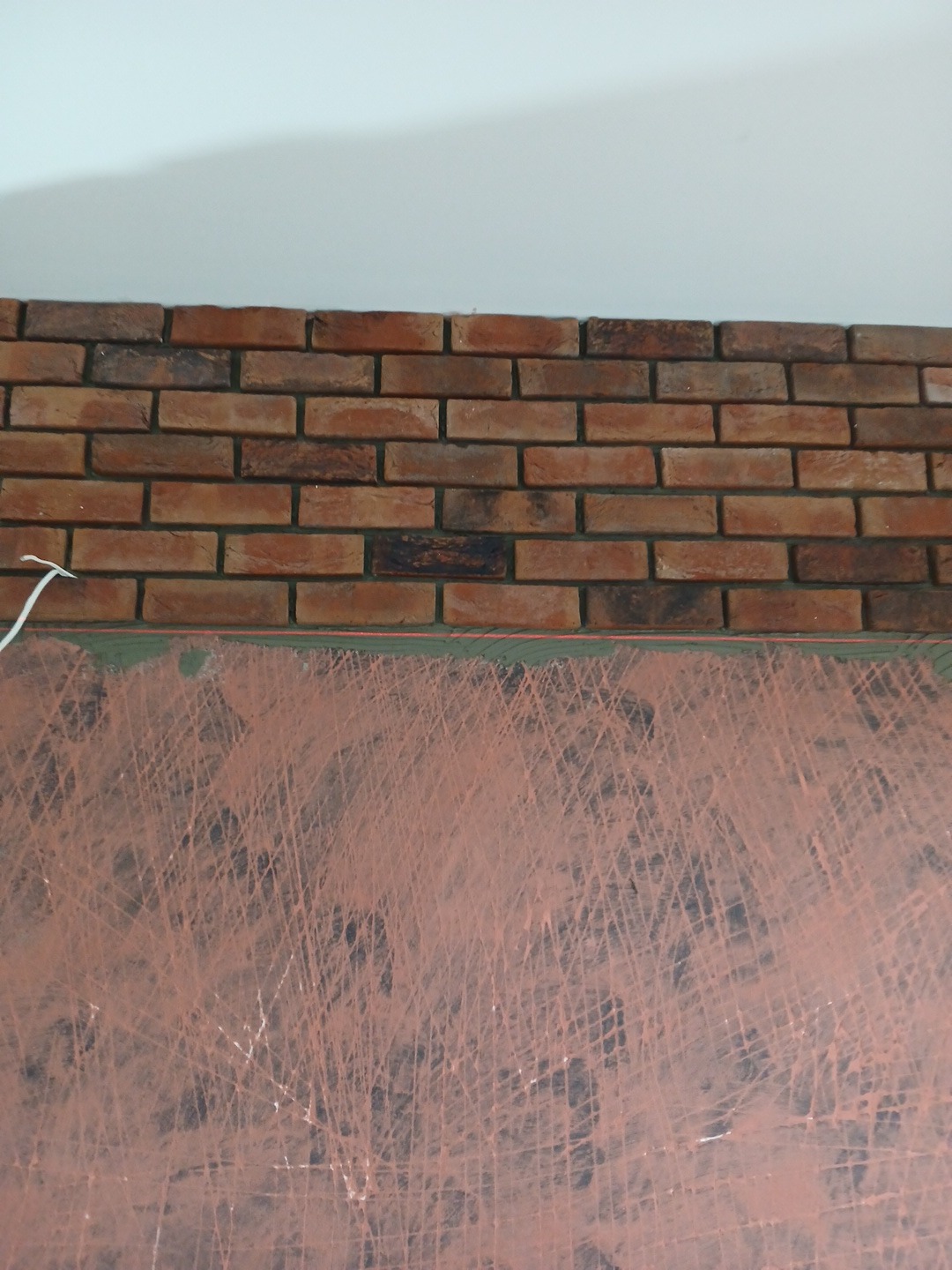 Fragment ściany z częściowo ułożoną dekoracyjną cegłą klinkierową nad przygotowanym podłożem z widocznymi śladami po szpachli.