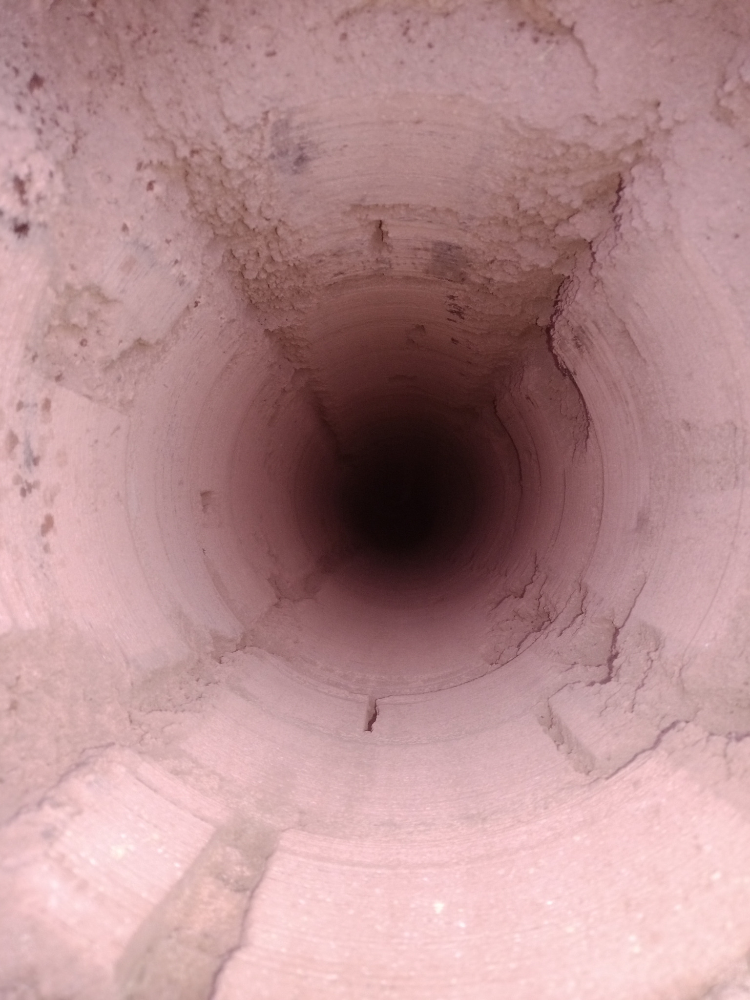 Wnętrze ceramicznego przewodu kominowego, widok od dołu ku górze, z widocznymi osadami i nierównościami na ścianach.