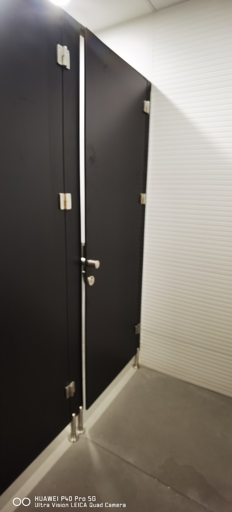 Czarne kabiny toaletowe z metalowymi okuciami i nogami w nowocześnie wykończonej łazience biurowej z białymi ścianami.