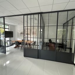 NFB INVEST SP. Z O.O. - Nowoczesne biuro z przeszklonymi ścianami działowymi w czarnych ramach, widoczny stół konferencyjny i stanowiska pracy.