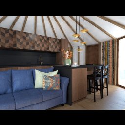NFB INVEST SP. Z O.O. - Wnętrze jurty z nowoczesnym aneksem kuchennym: niebieska sofa, drewniane wykończenie szafek kuchennych w jodełkę, czarny blat, barowe krzesła i ozdobne lampy wiszące.