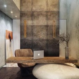 NFB INVEST SP. Z O.O. - Nowoczesne biuro domowe z drewnianym biurkiem, kamienną podstawą, betonową ścianą i minimalistycznymi złotymi akcentami oświetleniowymi.