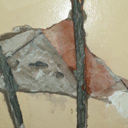 NFB INVEST SP. Z O.O. - Wypełnione szpachlą pionowe bruzdy w uszkodzonej ścianie z fragmentami cegły i betonu, przygotowane do dalszych prac wykończeniowych.