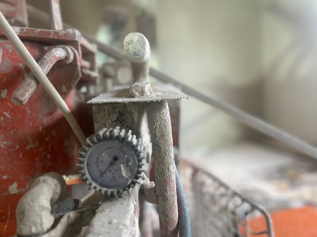 Detail zdjęcia maszyny do natryskowego nakładania gładzi, z widocznym manometrem i śladami zaschniętej masy szpachlowej.