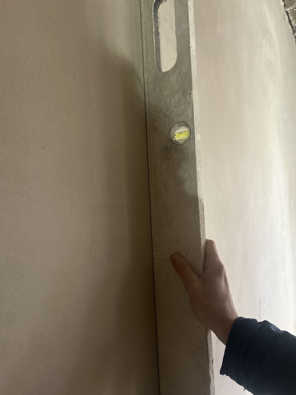 Sprawdzanie pionu ściany po szpachlowaniu za pomocą poziomicy, widoczna dłoń przytrzymująca narzędzie.