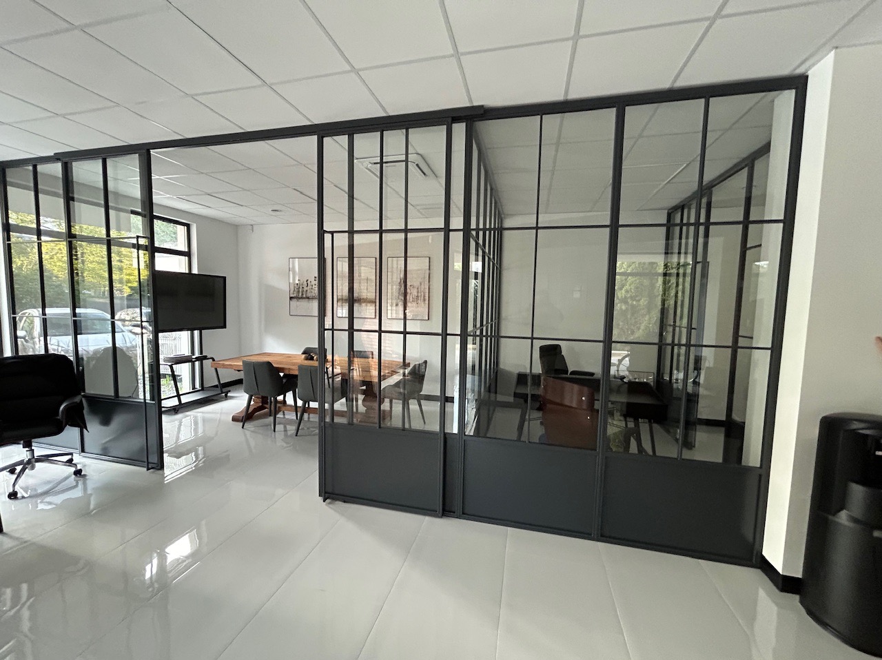 Nowoczesne biuro z przeszklonymi ścianami działowymi w czarnych ramach, widoczny stół konferencyjny i stanowiska pracy.