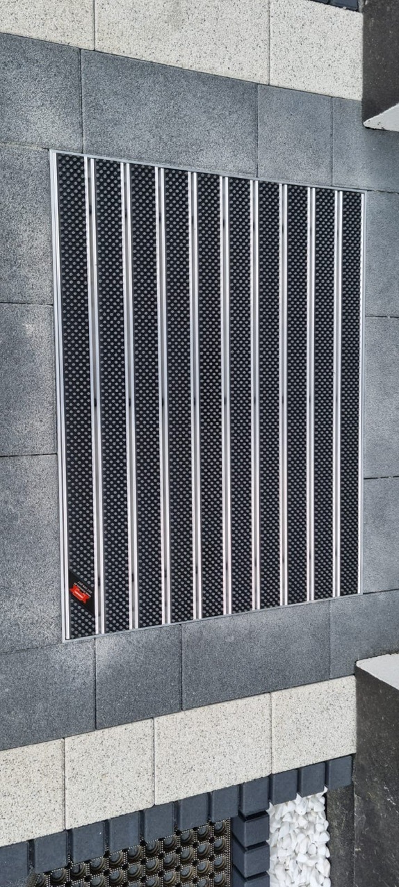 Wpuszczona wycieraczka systemowa z aluminiowymi profilami i czarnym wkładem czyszczącym, zamontowana w nawierzchni z kostki brukowej w Szczecinie.