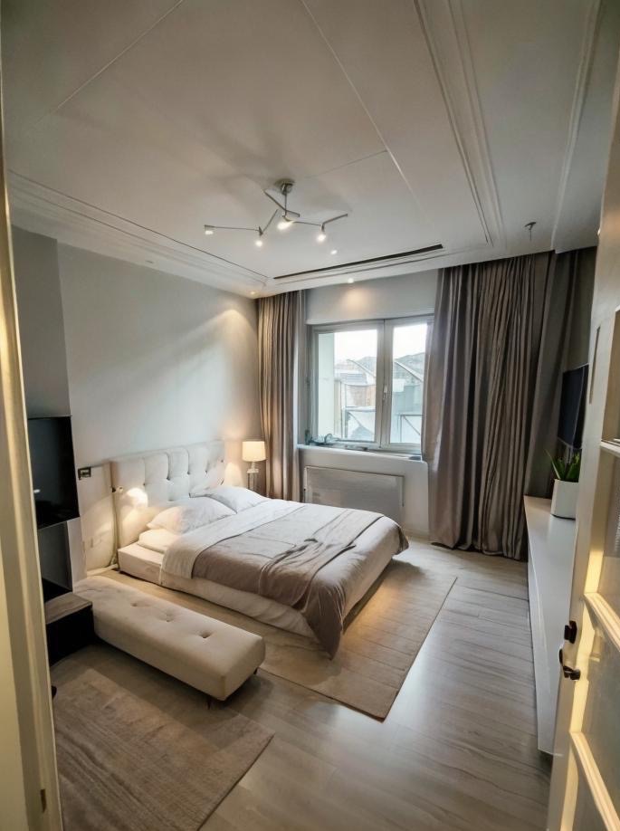 Jasna sypialnia z łóżkiem typu platforma, beżową narzutą i puszystym dywanem, widziana z perspektywy drzwi, z oświetleniem sufitowym w stylu industrialnym.