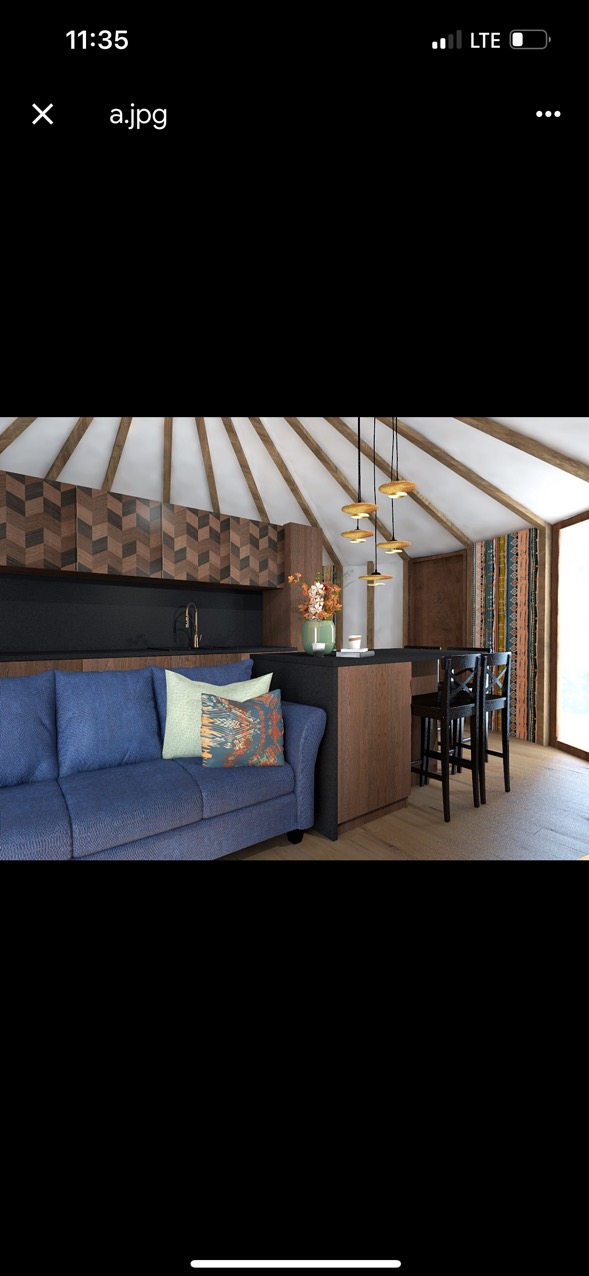 Wnętrze jurty z nowoczesnym aneksem kuchennym: niebieska sofa, drewniane wykończenie szafek kuchennych w jodełkę, czarny blat, barowe krzesła i ozdobne lampy wiszące.