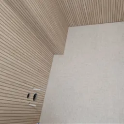 Ściana wykończona panelami drewnopodobnymi z widocznymi otworami na instalacje oraz fragment ściany wyłożony jasnymi, teksturowanymi płytkami.