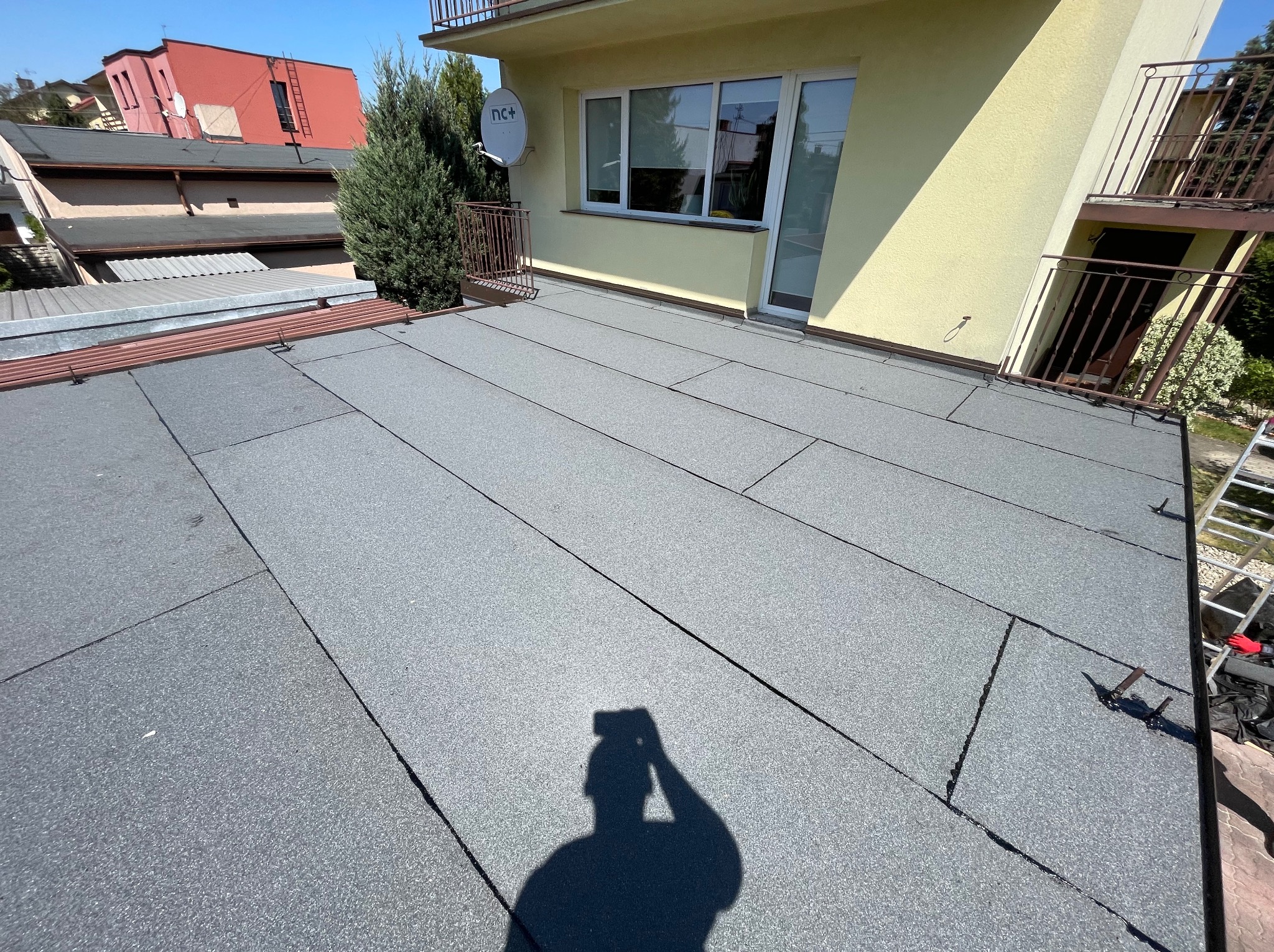 Nowe pokrycie dachu z papy bitumicznej na płaskim dachu budynku mieszkalnego, widoczny cień fotografa.