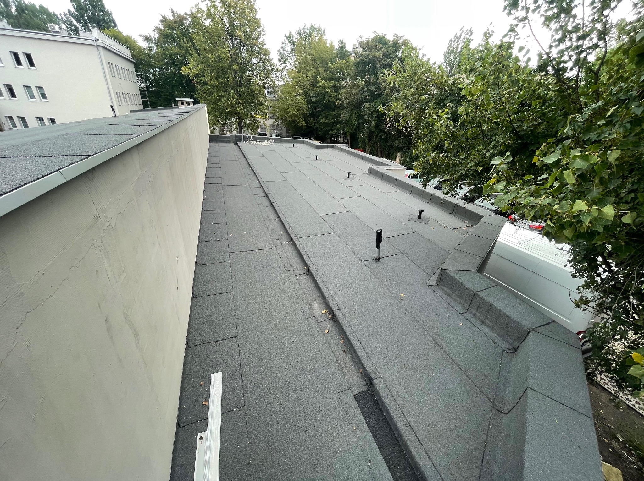 Dach pokryty papą termozgrzewalną na budynku wielorodzinnym, widok z góry, z widocznym kominem i elementami wentylacyjnymi.