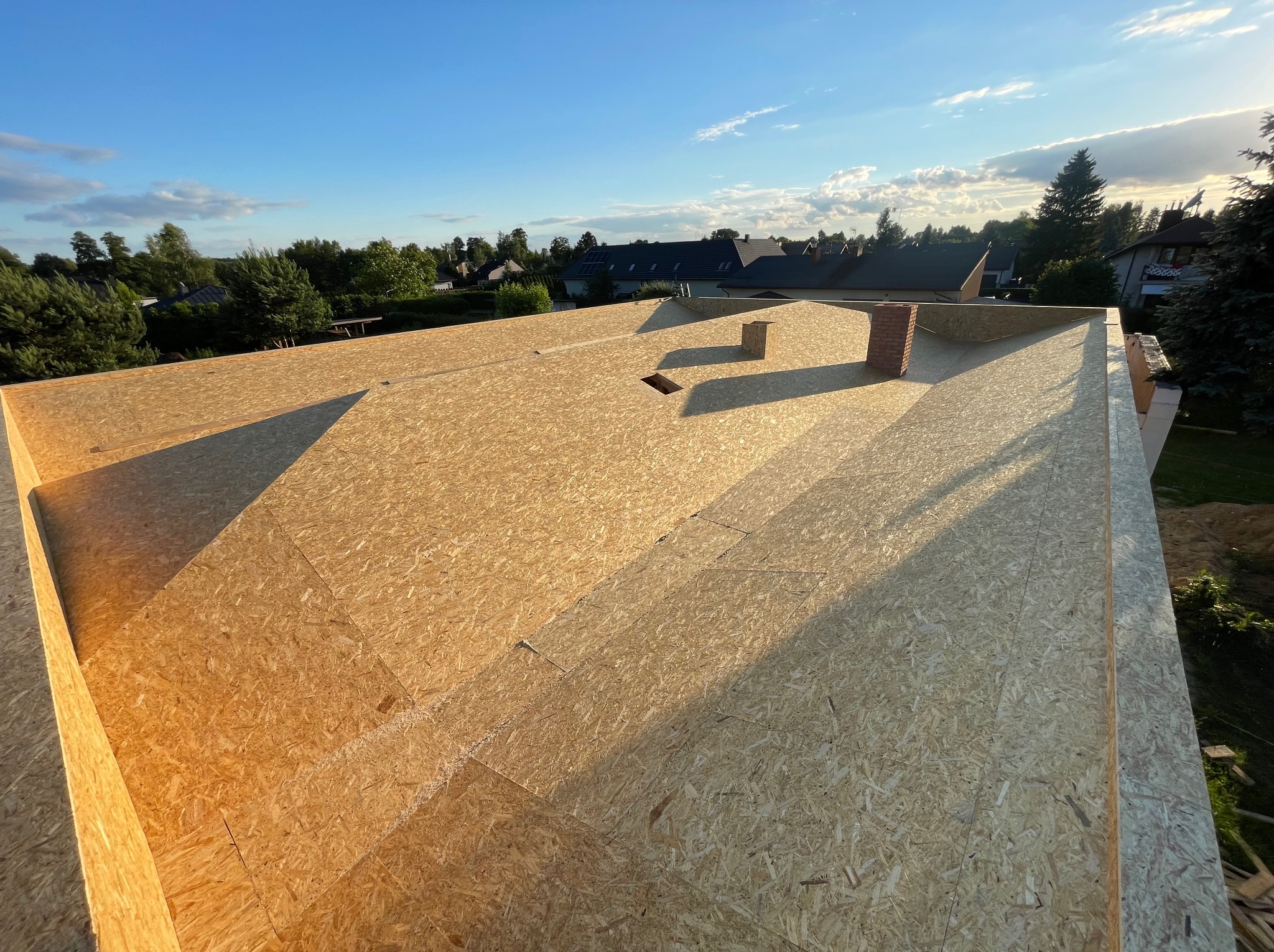 Wymiana dachu z płyt OSB w Mogilnie Dużym, widok z góry na konstrukcję przed położeniem pokrycia, komin z cegły klinkierowej w tle, słoneczny dzień.