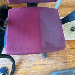 Duo-Partner Anna Sitarczyk - Krzesło biurowe z bordową tapicerką, widoczna różnica w czystości połowy siedziska po praniu ekstrakcyjnym, obok odkurzacz piorący i wąż ssący na drewnianej podłodze.