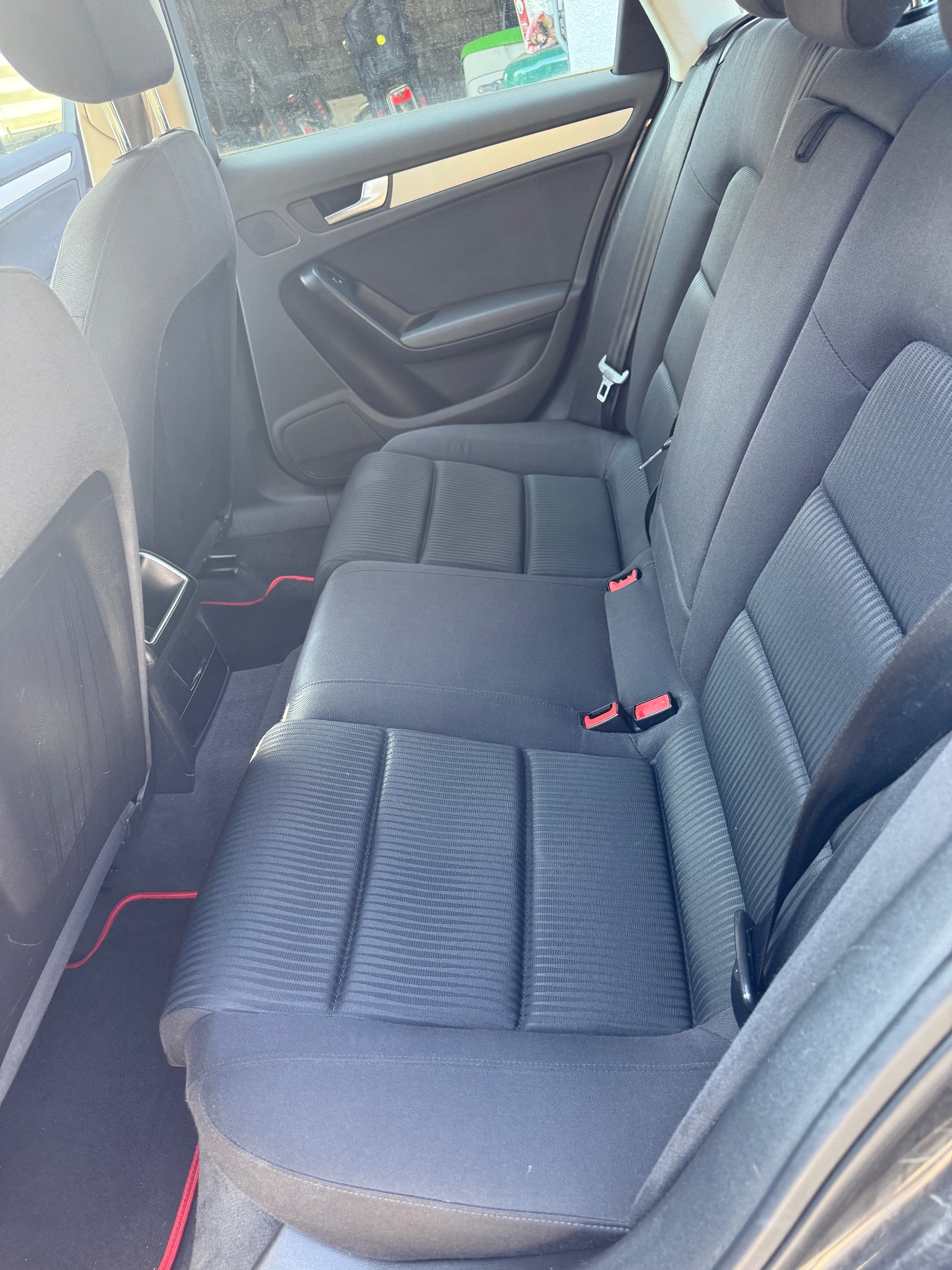 Wnętrze samochodu z widocznymi tylnymi siedzeniami z ciemną tapicerką i czerwonymi akcentami na dywanikach.