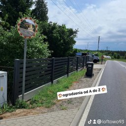 Tomasz Nabagło - Nowoczesne, poziome ogrodzenie metalowe w kolorze grafitowym, z widocznym betonowym podmurówką. W tle droga, samochód i osoba. Lustro drogowe odbija budynek.