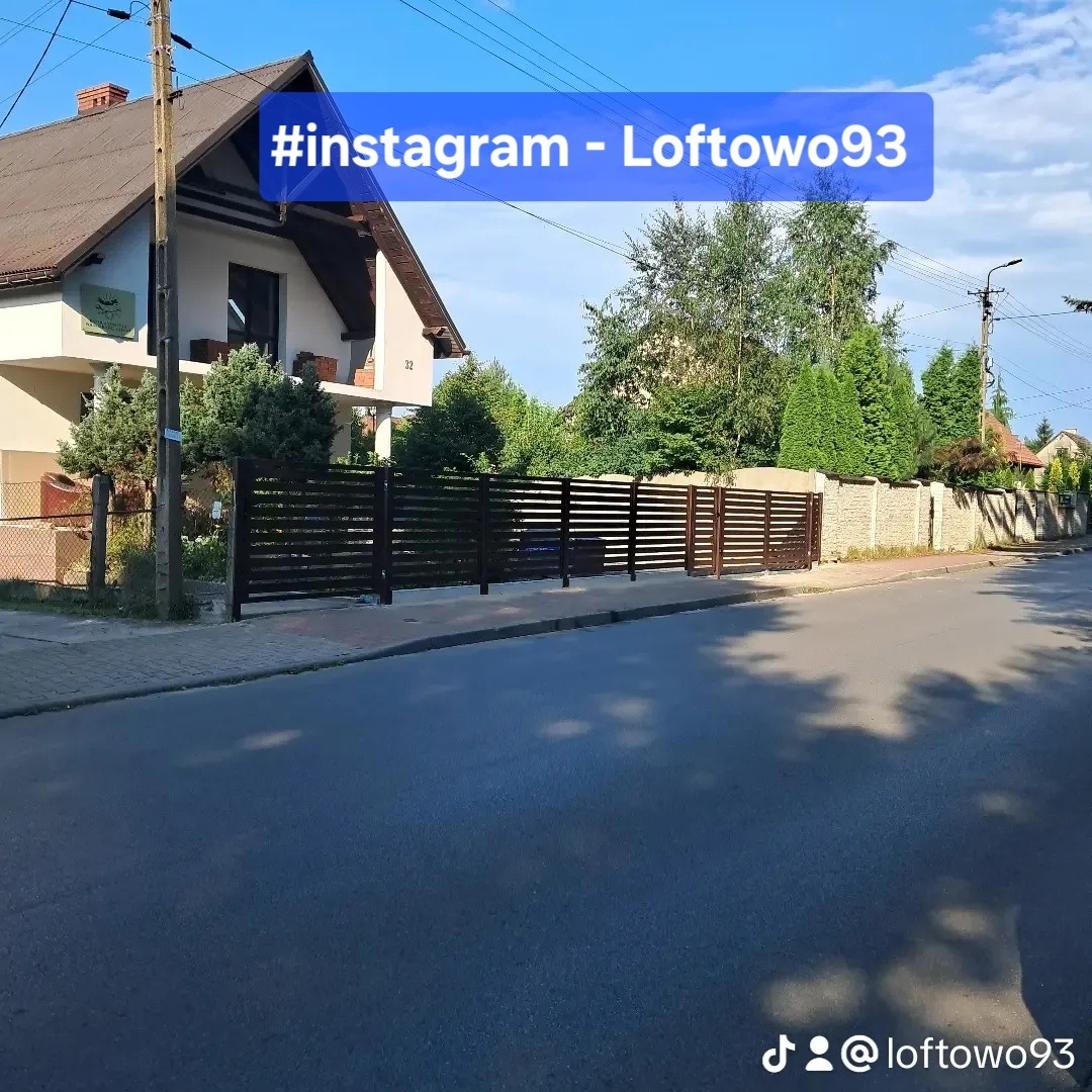 Nowoczesne ogrodzenie posesji z poziomych, brązowych paneli metalowych, widok z ulicy w słoneczny dzień. Fragment domu w tle.