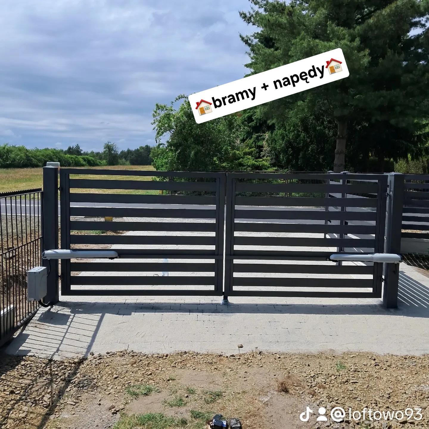 Nowoczesna, pozioma brama metalowa w kolorze antracytowym z automatycznym napędem, widoczna na tle zieleni. Minimalistyczny design, symetryczny układ.