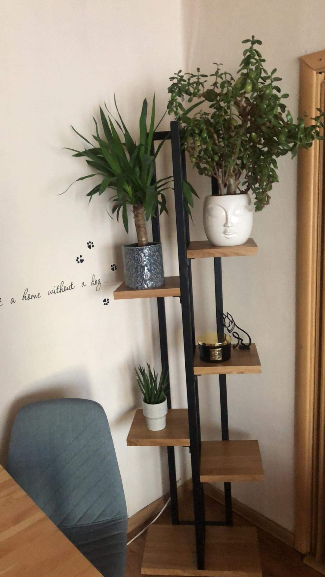 Metalowy regał na kwiaty z drewnianymi półkami, na których stoją rośliny doniczkowe i dekoracje. Minimalistyczny design, czarne ramy, jasne drewno, domowe wnętrze.