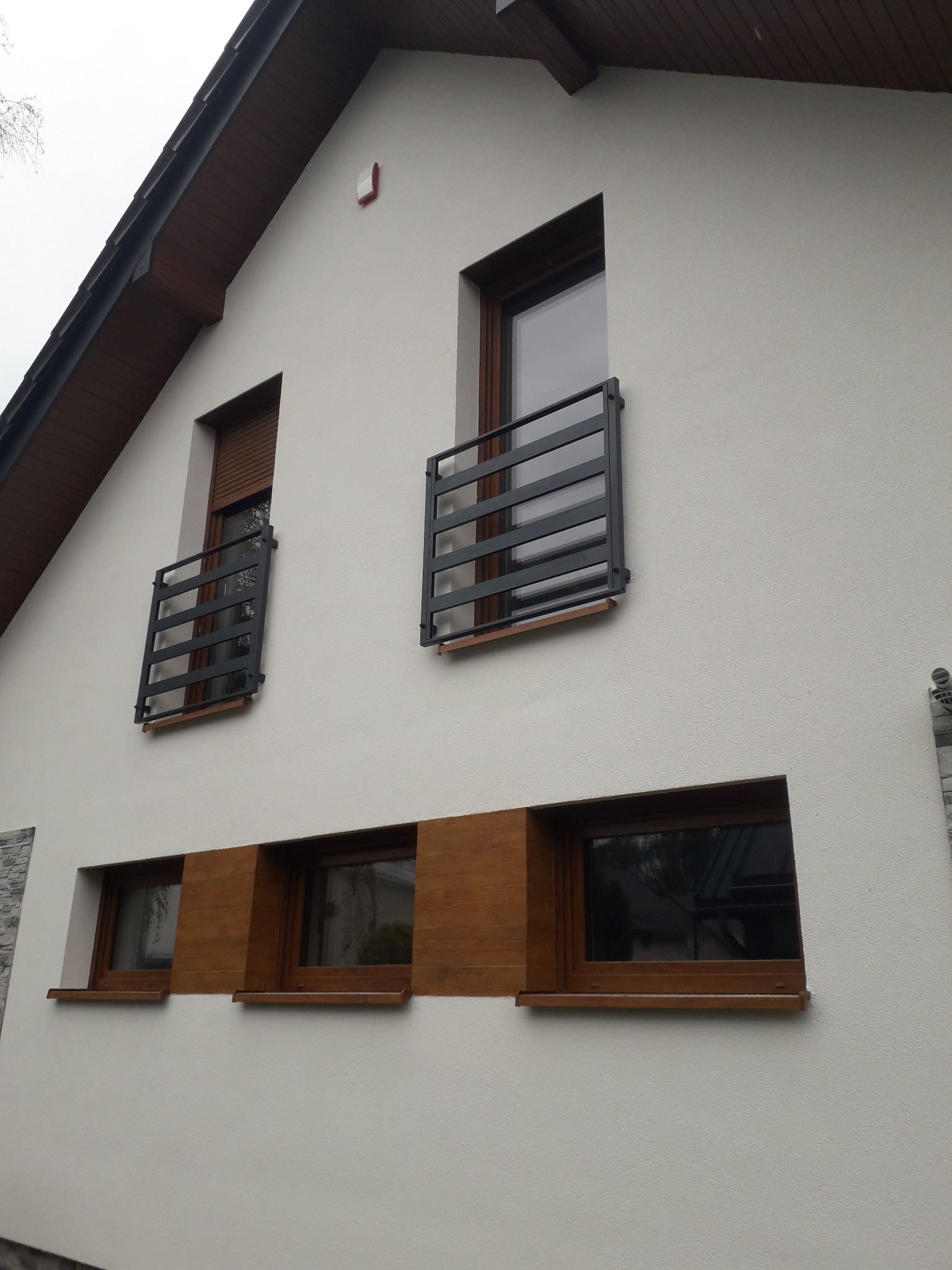 Elewacja domu z oknami i nowoczesnymi, metalowymi balustradami okiennymi w kolorze grafitowym. Widok z dołu, podkreślający minimalistyczny design.