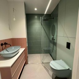 Vinci Art Mikrocement - Nowoczesna łazienka w odcieniach zieleni i różu z umywalką nablatową w kształcie misy, kabiną prysznicową walk-in z zielonymi płytkami oraz podwieszanym WC w kolorze ścian, w trakcie wykańczania...