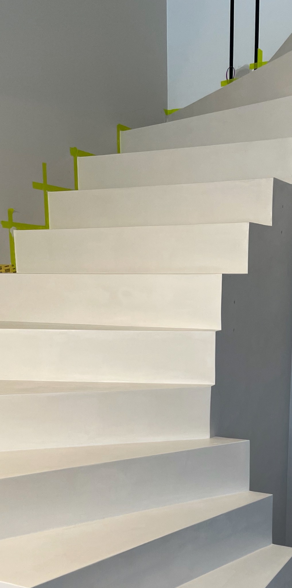 Białe schody z prostymi stopniami, zabezpieczone żółtą taśmą malarską w narożnikach, minimalistyczny design.