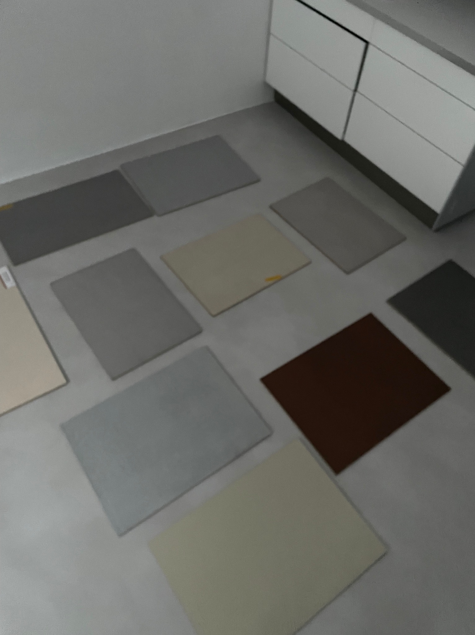 Różnokolorowe próbki materiałów posadzkowych ułożone na podłodze w pobliżu białych szafek kuchennych.