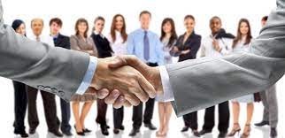 Uścisk dłoni na tle zespołu w strojach biznesowych, symbolizujący współpracę i partnerstwo.