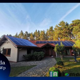 ECOAUTOMATION DAWID I WOJCIECH ZAHRT SPÓŁKA CYWILNA - Dom jednorodzinny z panelami słonecznymi na dachu, widoczny instalator przy trawniku, błękitne niebo w tle, logo firmy w dolnej części zdjęcia.