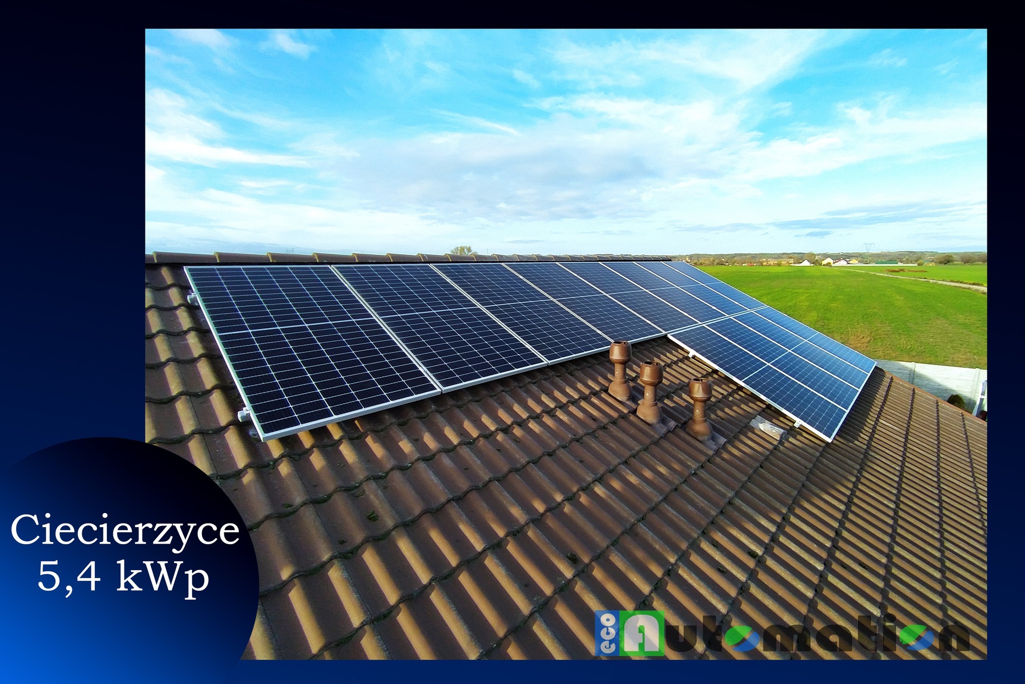 Panele słoneczne zamontowane na brązowym dachu z dachówki ceramicznej, widok z góry na tle błękitnego nieba z chmurami i zielonych pól w oddali.