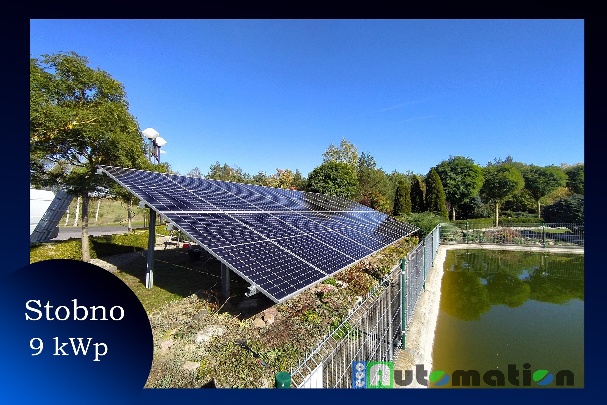 Instalacja paneli słonecznych o mocy 9 kWp w Stobnie, widoczna z metalowego ogrodzenia, z zielenią i stawem w tle pod błękitnym niebem.