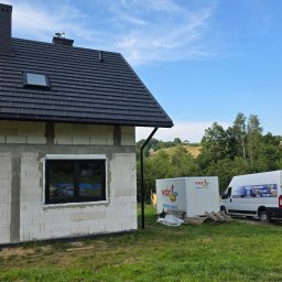 Przedsiębiorstwo Produkcyjno-Handlowo-Usługowe Prime Home Daniel Paździora - Dom w budowie z zamontowanym oknem PCV w czarnej ramie, obok zaparkowany biały bus firmy oferującej okna, drzwi i bramy. Dach pokryty czarną dachówką.