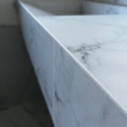 Robert Hodyjas MHR - Fragment blatu umywalki z białego marmuru z widoczną fugą, zamontowany w łazience.