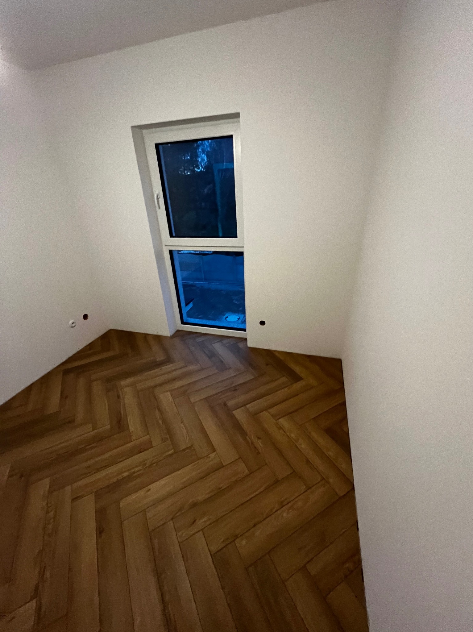 Ułożona pod kątem 45 stopni podłoga z paneli winylowych imitujących drewno w odcieniach brązu, widoczna w rogu pokoju z oknem.