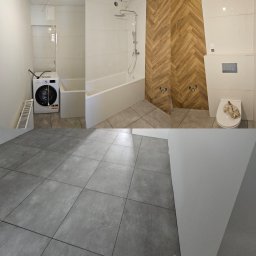 MSW Michał Sielski Wykończenia - Częściowo wykończona łazienka z drewnopodobną ścianą w jodełkę, białą wanną, toaletą z deską i pralką, szare płytki podłogowe, widoczne instalacje wodne.