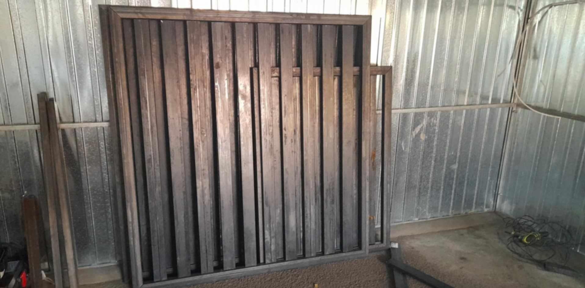 Surowa, metalowa konstrukcja bramy lub ogrodzenia z pionowymi profilami, w warsztacie z blachy falistej.