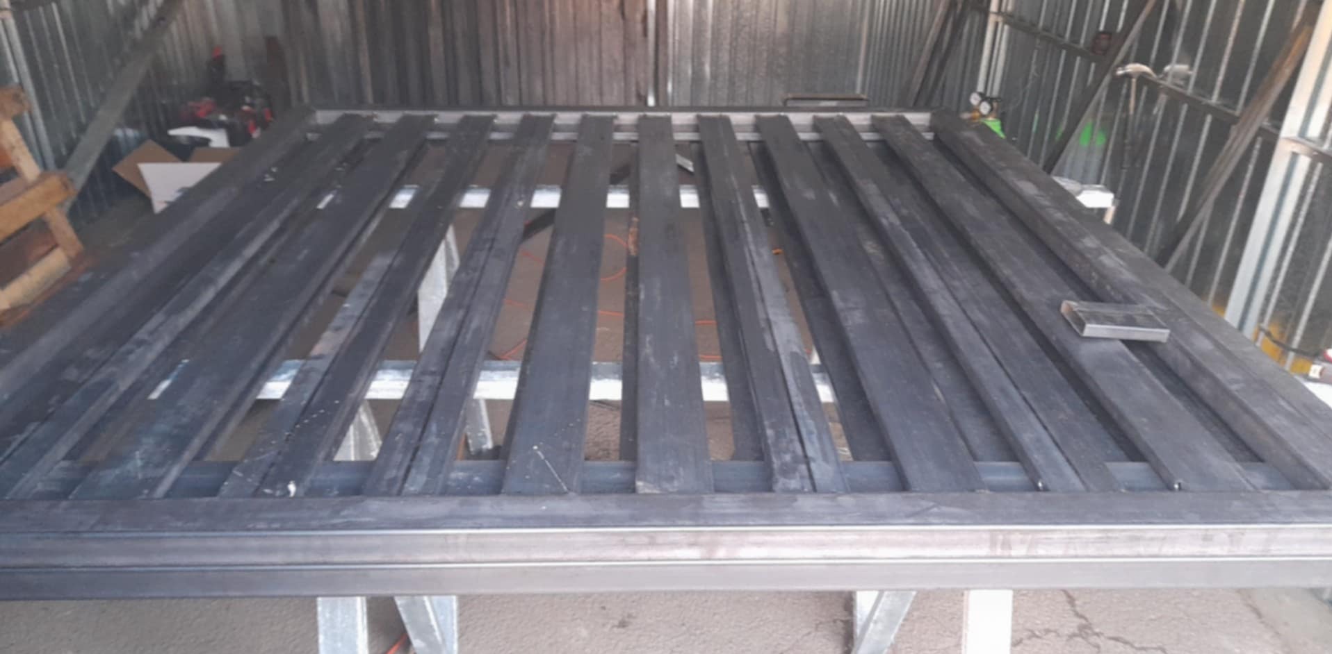 Element metalowej konstrukcji, prawdopodobnie brama lub fragment ogrodzenia, w trakcie spawania w warsztacie.