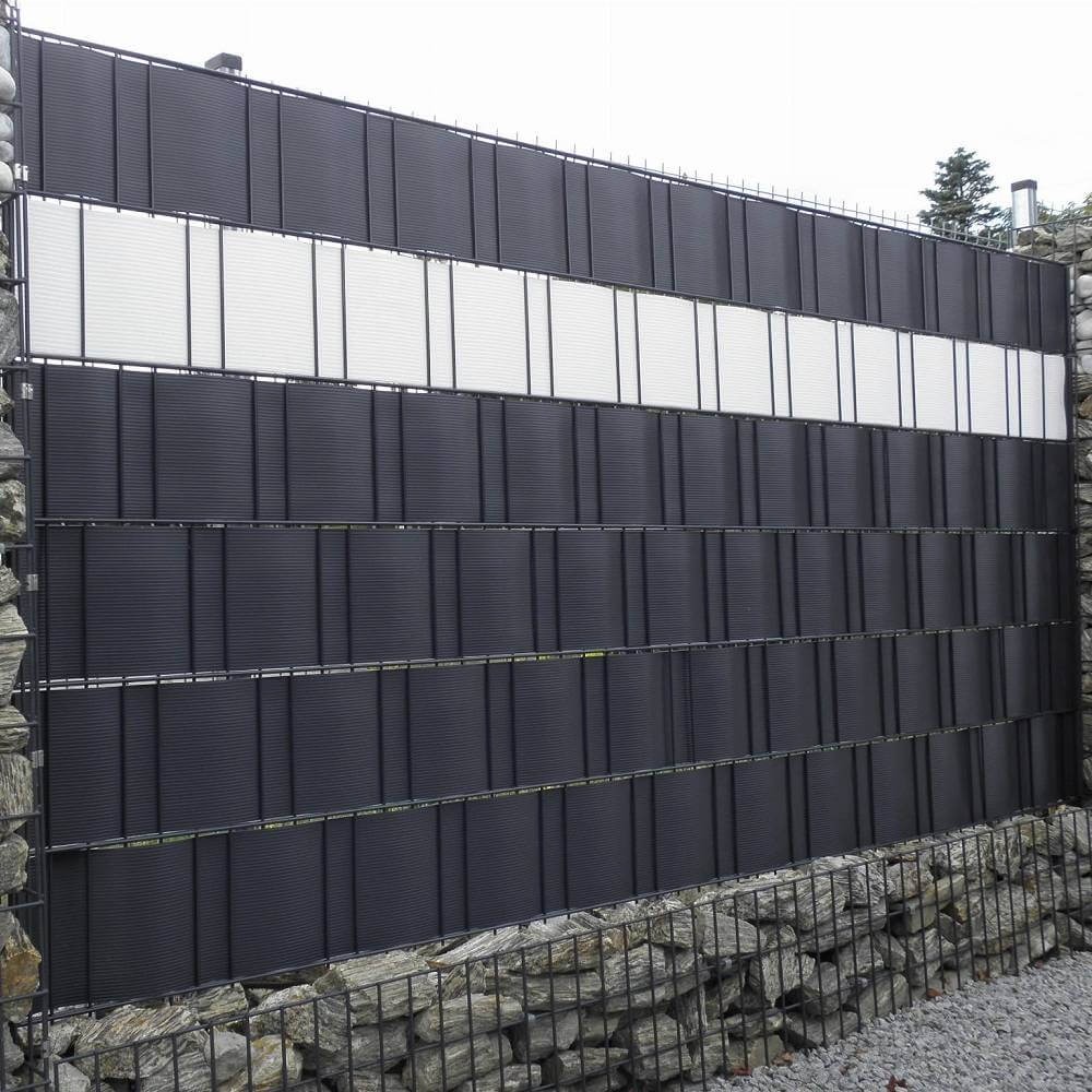 Nowoczesne ogrodzenie z czarnymi panelami z poziomymi paskami i białym pasem pośrodku, osadzone na kamiennym fundamencie w metalowej siatce.