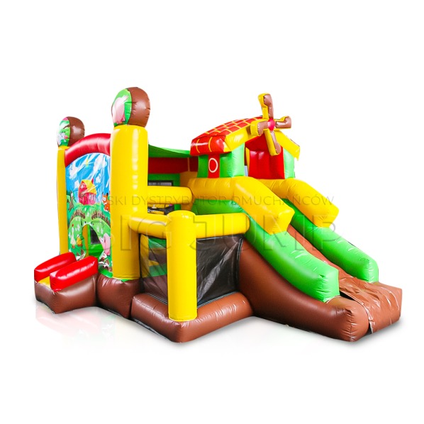 Kolorowy dmuchany zamek z motywem wiejskim, zjeżdżalnią i elementami dekoracyjnymi imitującymi wiatrak.