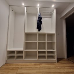 F.H.U KRZYSZTOF KLIMCZAK - Biała, otwarta szafa wnękowa z półkami i drążkiem, oświetlona punktowo, z kurtką wiszącą na drążku, na podłodze panele imitujące drewno, widok z dołu.