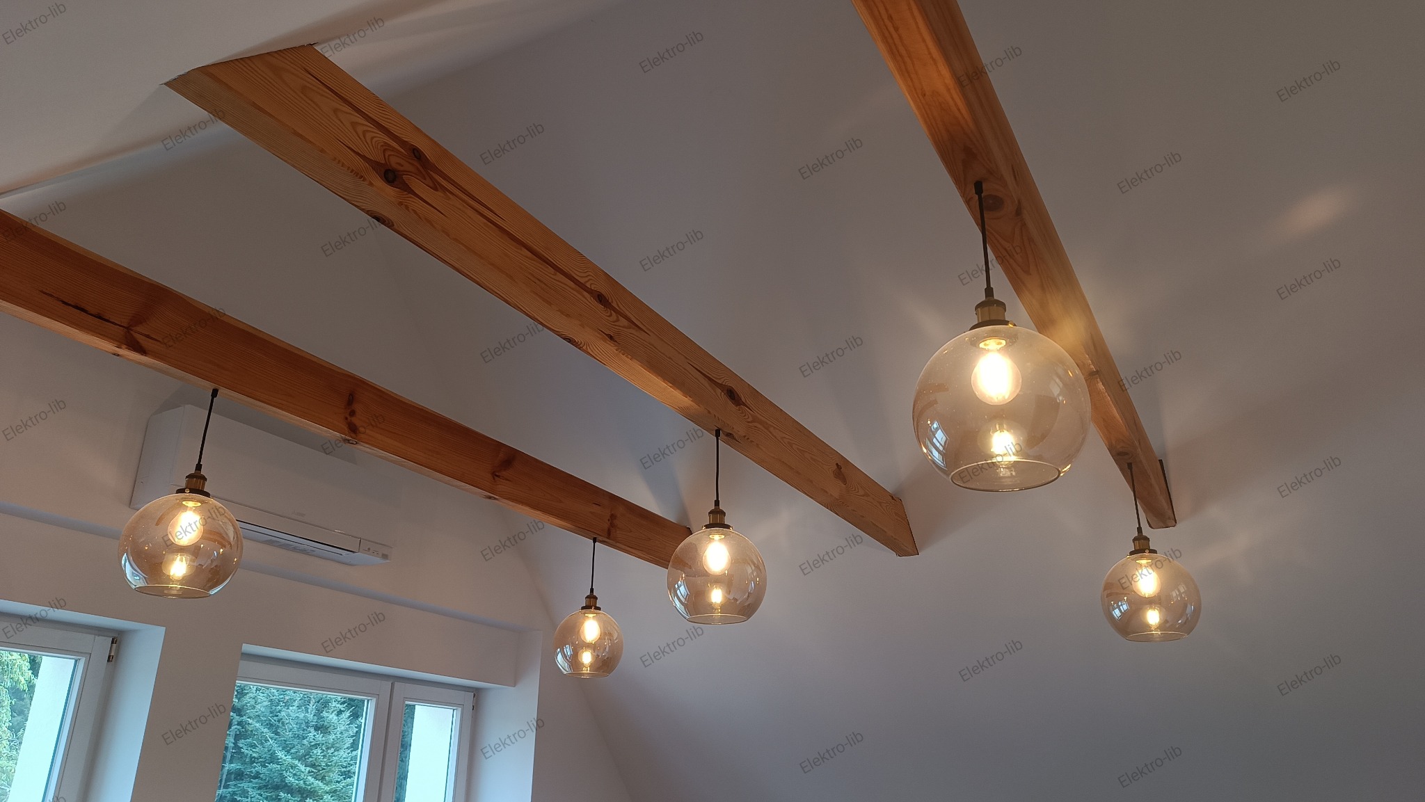 Nowoczesne oświetlenie sufitowe: Szklane kule zawieszone na czarnych przewodach, zamontowane na drewnianych belkach w jasnym wnętrzu, widok z dołu.