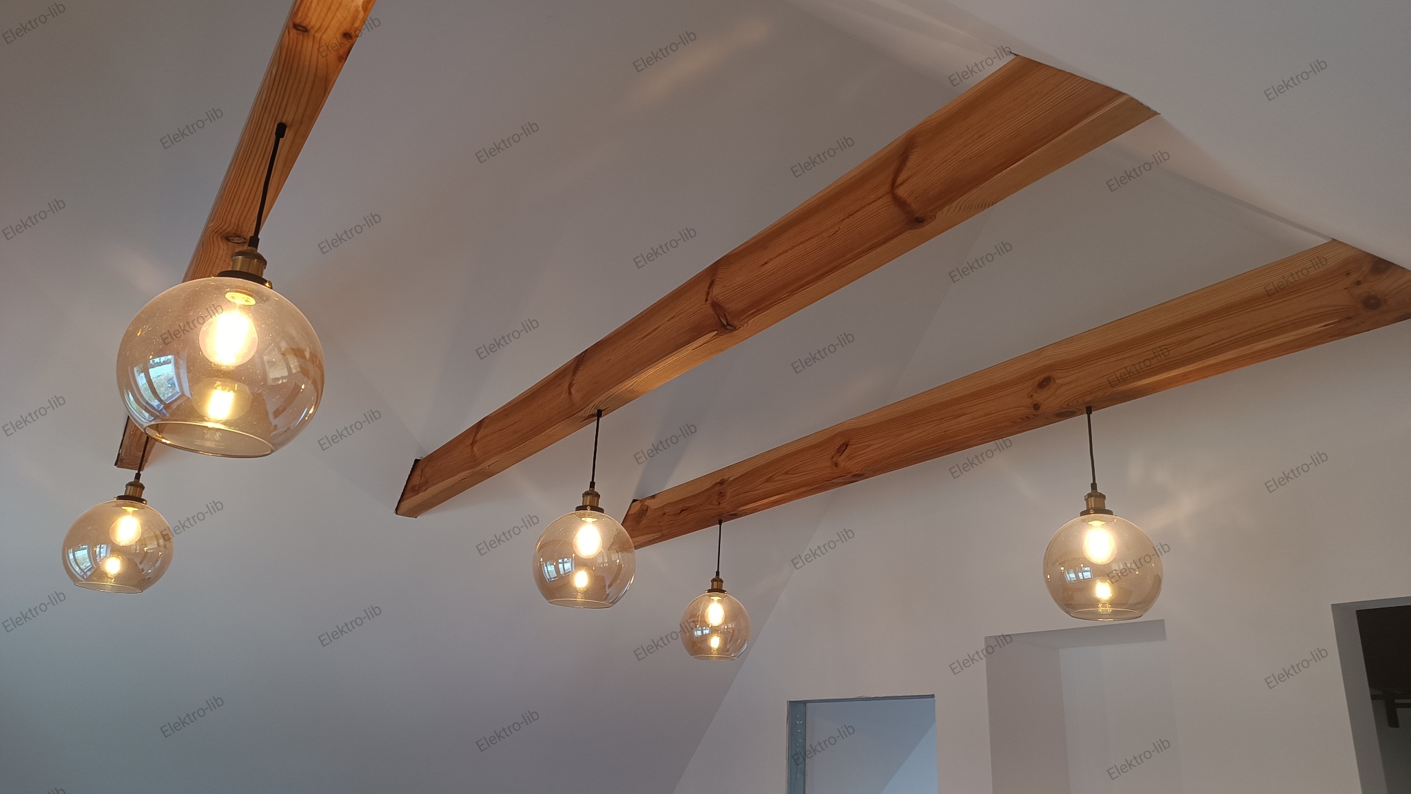 Szklane, kuliste lampy wiszące z żarówkami Edison, zamontowane na drewnianych belkach stropowych w nowoczesnym wnętrzu.