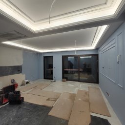 GWARANT - WOWA VOLODYMYR MELNYK - Pokój w trakcie prac wykończeniowych: pomalowane na błękitno ściany z dekoracyjnymi listwami, marmurowe płytki podłogowe częściowo zakryte kartonem, sufit z oświetleniem LED i dekoracyjnymi...
