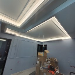 GWARANT - WOWA VOLODYMYR MELNYK - Wykończony sufit z oświetleniem LED w niebieskim pokoju, widoczne kartony i narzędzia budowlane świadczące o trwających pracach wykończeniowych.
