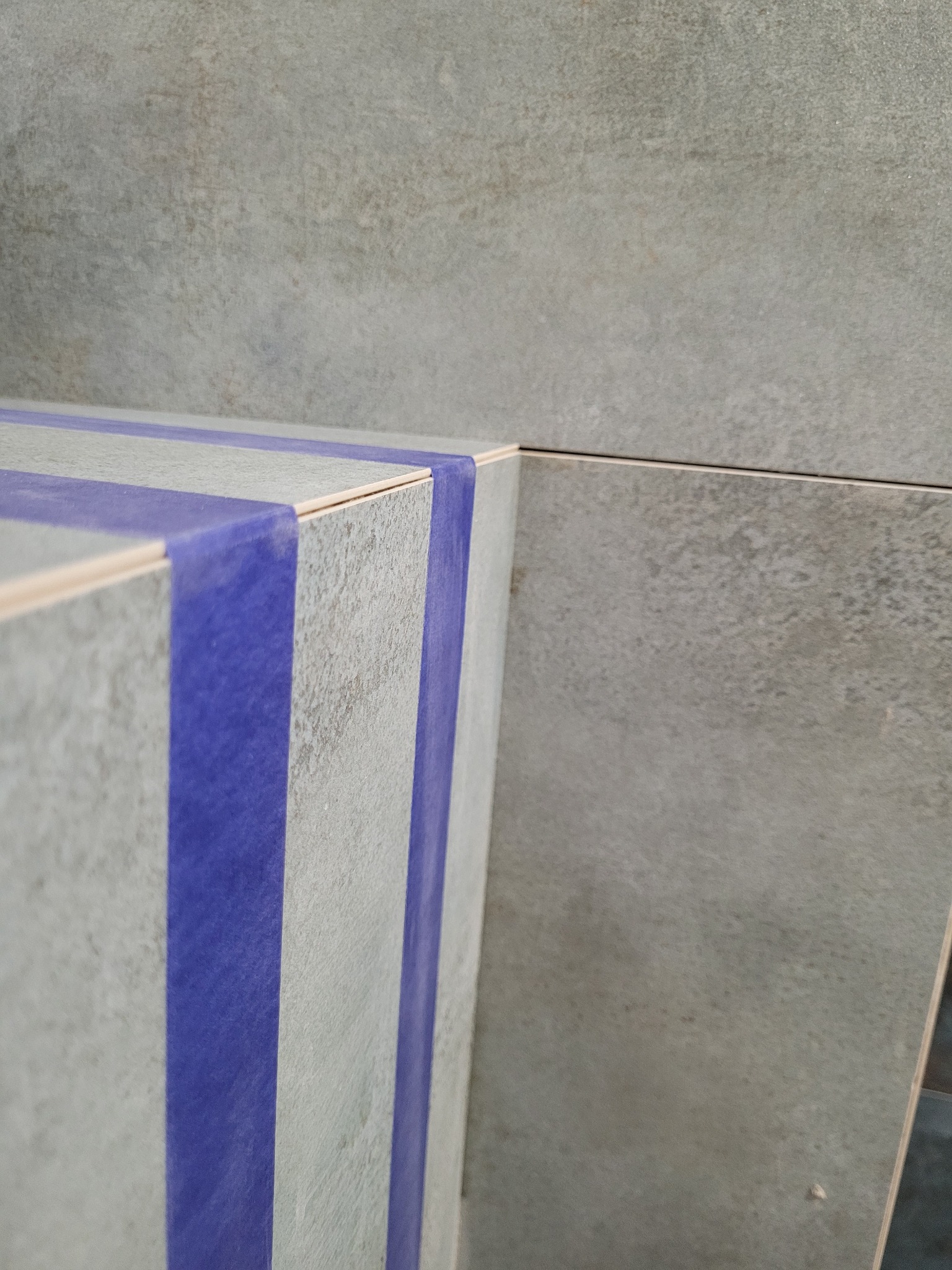 Szara, teksturowana płytka ścienna z niebieską taśmą malarską zabezpieczającą krawędzie podczas prac wykończeniowych.