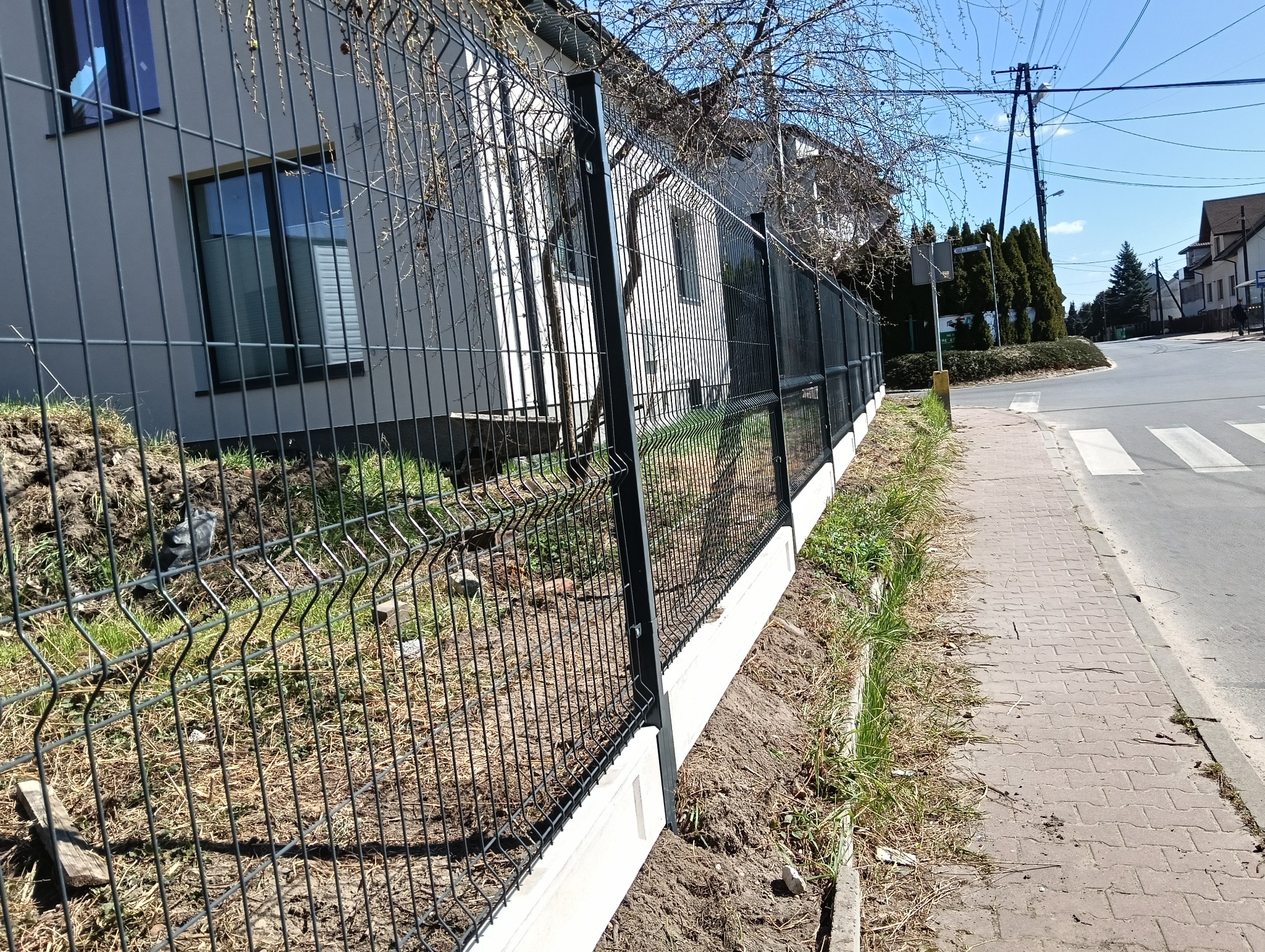 Nowoczesne ogrodzenie panelowe z podmurówką betonową, widok z boku na tle domu jednorodzinnego i chodnika.